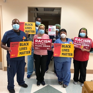 Group of nurses in hospital hold signs "Racism is a Public Health Crisis" and "Black Lives Matter"