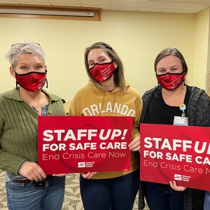 Three nurses inside hold signs "Staff Up for Safe Care"