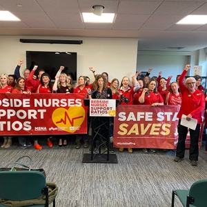 Large group of nurses with raised fists, holding banner "Bedside Nurses Support Ratios"