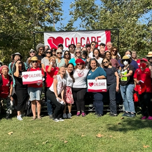 Large group of people in park standing and sitting in front of CalCare banner, some holding CalCare signs