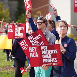 Nurses on picket line outside hospital holding signs "Hey HCA Put Patients Over Profit"
