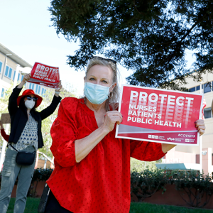 Nurses outside hospital hold signs "Protect Nurses, Patients, Public Health"