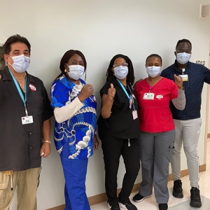 Group of five nurses inside hospital giving thumbs up