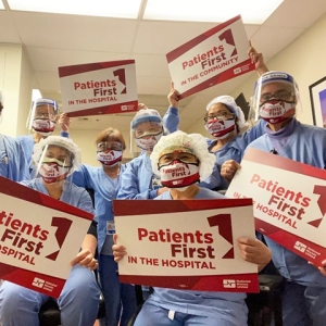 Large group of nurses inside hospital hold signs "Patients First"