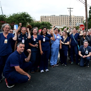 Large group of nurses outside hospital with raised fists