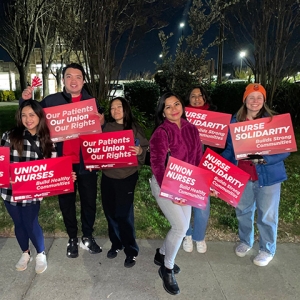 Group of nurses outside hospital at night, holding signs and banner "Our Patients, Our Union, Our Rights"