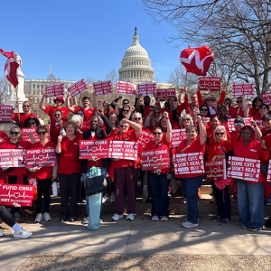 Seven nurses standing in front of U.S. capitol building, smiling, with raised fists, holding signs "Some Cuts Don't Heal"