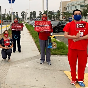 Nurses hold signs "Save Lives" and variations "Hands Off Our Ratios" "Safe Staffing Now" "PPE Now"