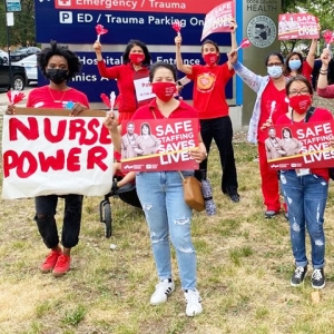 Nurses and community outside Cook County ER with signs "Safe Staffing Saves Lives" and "Nurse Power"