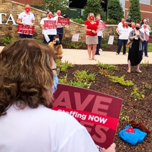 Nurses outside Mission facility holding event, sign in foreground "Save Lives, (Safe) Staffing Now"