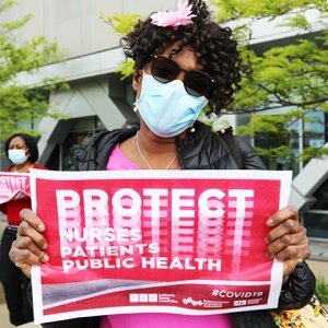 Nurse holding sign with "Protect Nurses/Patients/Publich Health"