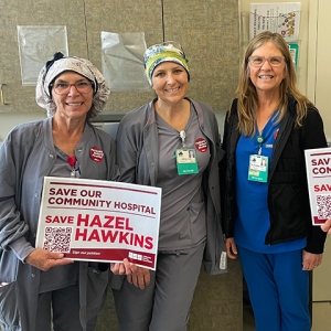 Three nurses hold signs "Save Our Community Hospital: Save Hazel Hawkins"