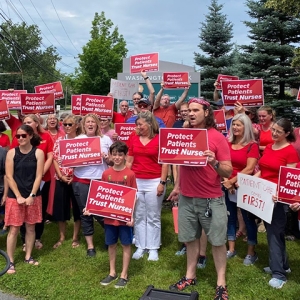 arge group of nurses in front of camera holding signs "Protect Patients, Trust Nurses"