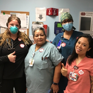 Group of five nurses inside hospital giving thumbs up