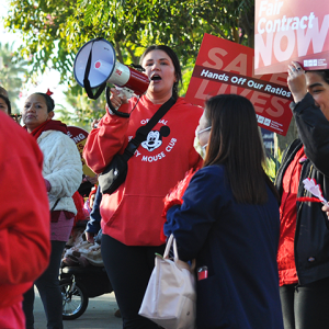Long Beach nurses at action, with bullhorn, signs that say "Fair Contract Now" and "Save Lives: Hands off our Ratios!"