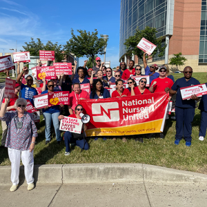 Nurses in front of St Agnes with signs: "RN Safe Staffing saves lives" and "Patients 1st in the hospital" and a "Natioanal Nurses United" banner
