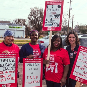Four nurses standing outside smiling, holding signs calling for a fair contract