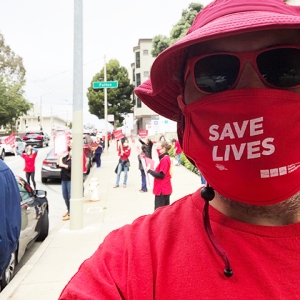Nurses on strike on street, one with mask "Save Lives"