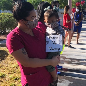 Nurse holding toddler with sign "Protect My Mommy"