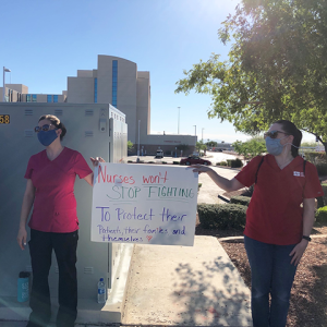 Nurses outside hold sign "Nurses won't stop fighting to protect their patients"