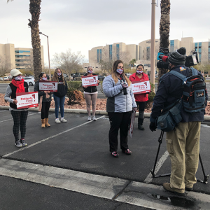 Nurses hold signs "Patients First" in front of TV camera