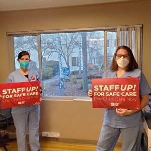 Two nurses inside hospital hold signs "Staff Up For Safe Care"