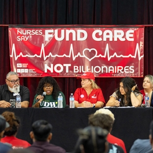 Panel at town hall in front of banner "Fund Care Not Billionaires"