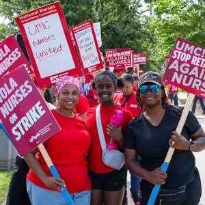 Three nurses side-by-side, smiling, holding signs calling out LCMC Health