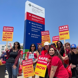 Group of nurses outside Providence Little Company of Mary Medical Center smiling and holding signs "Safe Staffing Now" and "Nurses Demand a Fair Contract Now"