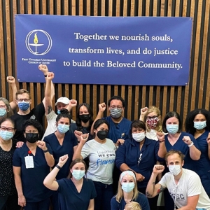 Large group of nurses with raised fists in front of sign "Together we nourish souls, transform lives, and do justice to build the Beloved Community