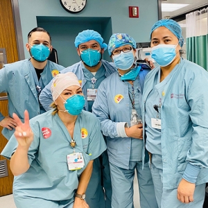 Group of five nurses inside hospital giving thumbs up