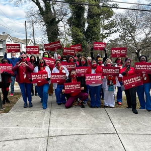 Large group of nurses outside holding signs "Staff Up for Safe Care"