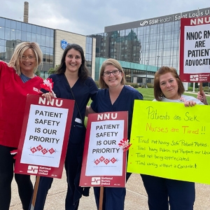 Group of four nurses outside Saint Louis University Hospital holding signs calling for patient safety