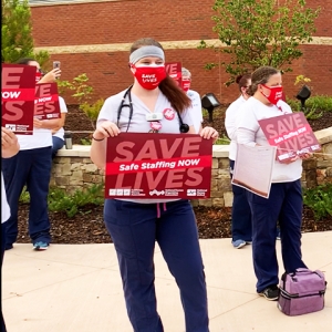 Nurses outside mission hospital hold signs "Save Lives: Safe Staffing Now"