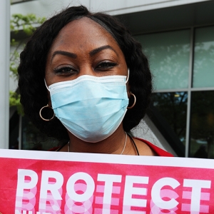 Nurse in mask holding sign: "PROTECT"