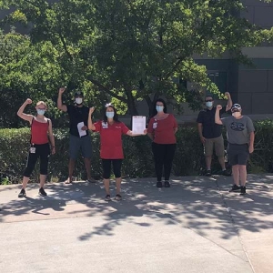 Large group of nurses outside hospital with fists raised