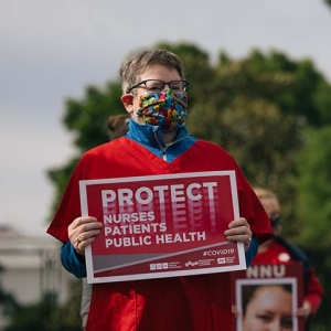 Masked nurse outside holds signs "Protect Nurses, Patients, Public Health"