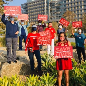 Group of healthcare workers outisde hopsital hold signs "Safe Staffing Now"