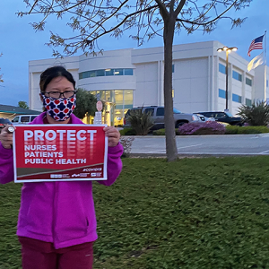 Nurse in front of Hazel Hawkins with sign "Protect Nurses, Patients, Public Health"