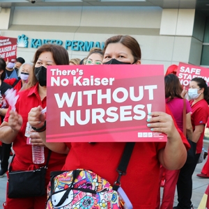 Nurse outside holds sign "There's no Kaiser without nurses"