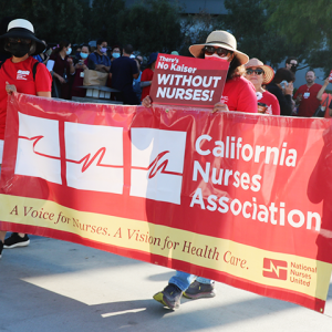 Nurses marching and holding CNA/NNU banner and signs at LAMC: "There's no Kaiser without nurses!"