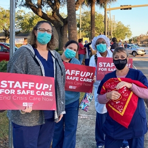 Group of four nurses outside hold signs "Staff up for safe care"