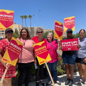 Group of six nurses outside hospital, smiling, holding signs "Nurses are the hear of patient care"