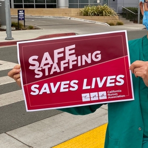 Nurse holds signs "Safe Staffing Saves Lives"