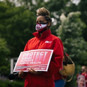 Masked nurse outside holds signs "Protect Nurses, Patients, Public Health"