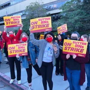 Group of nurses outside hold signs "Sutter RNs on Strike"