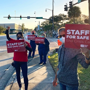 Group of four nurses outside hold signs "Staff up for safe care"