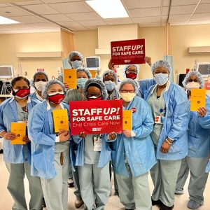 Large group of nurses inside hospital hold sign "Staff Up for Safe Care"