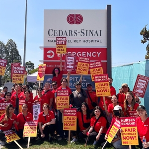 Nurses holding signs in front of Cedars-Sinai "Some cuts don't heal" and "Nurses demand a fair contract now"