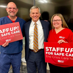 Two nurses standing with North Carolina Attorney General Josh Stein holding signs "Staff Up for Safe Patient Care"